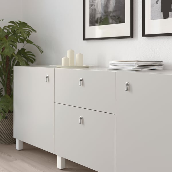 White cabinet with drop handles preventing damage, three candles, stack of magazines, framed pictures, green plant.