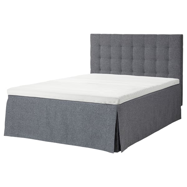 A gray MOSTERHAMN bed with tufted headboard, a white mattress, and a matching skirt, designed for comfortable sleep.