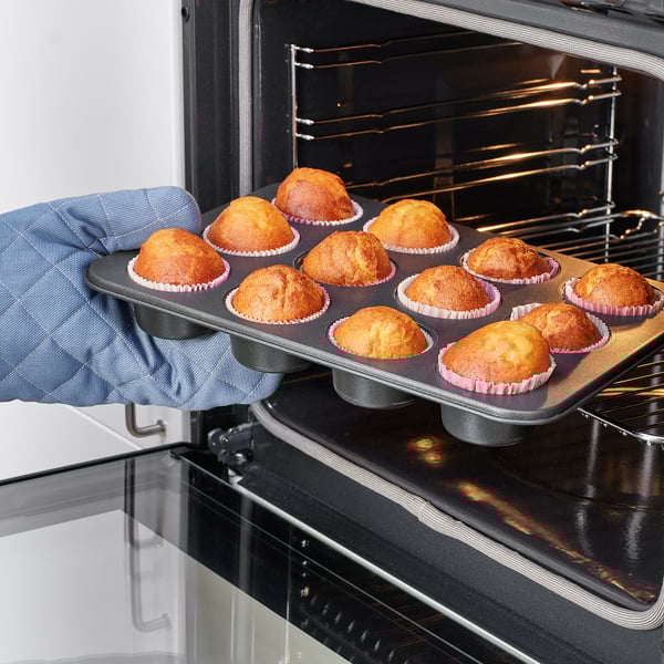 Person using oven mitts removing tray of baked muffins from oven.