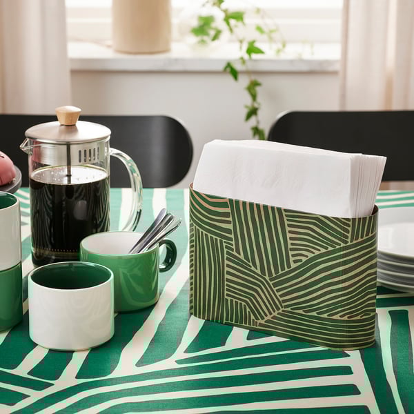 Table set with green-themed items: napkin holder, coffee press, mugs, and utensils.