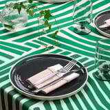 Green and white striped table setting with dark plates, rolled cutlery in a napkin, and glasses.