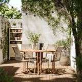 Outdoor patio set with round wooden table and black chairs under string lights.