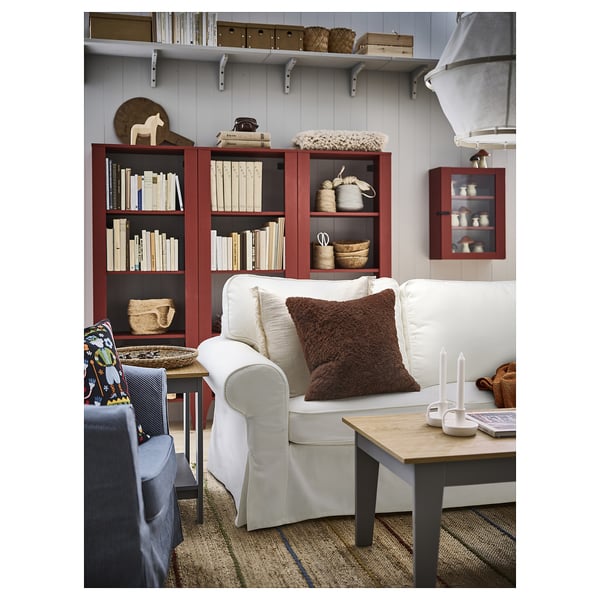A cosy living room with a plush white sofa, a brown cushion, wooden coffee table, and shelving units.