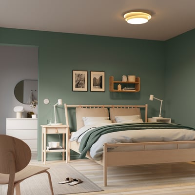 Modern green bedroom with light wood furniture. Large bed with white & green bedding, NÖSUND lamp, minimal decor, dresser, mirror, chair.