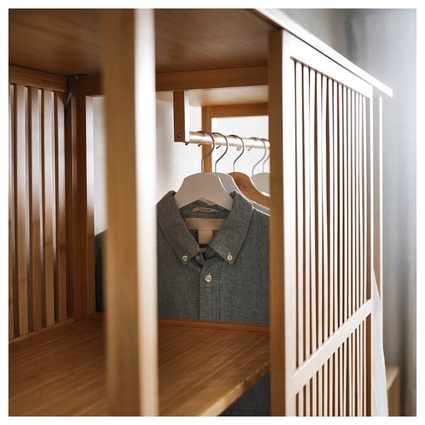 Scandinavian-style NORDKISA wardrobe in bamboo. Gray shirt hangs on a sliding door, dividing sides with open shelves.