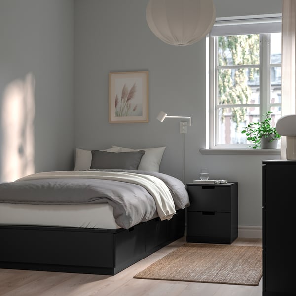 Minimalist bedroom NORDLI bed in black with white linens, gray wall, and large window. Artwork above bed, dark nightstand, and natural rug.