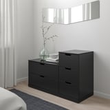 Black NORDLI chest of drawers under mirror, next to window, minimalist design.