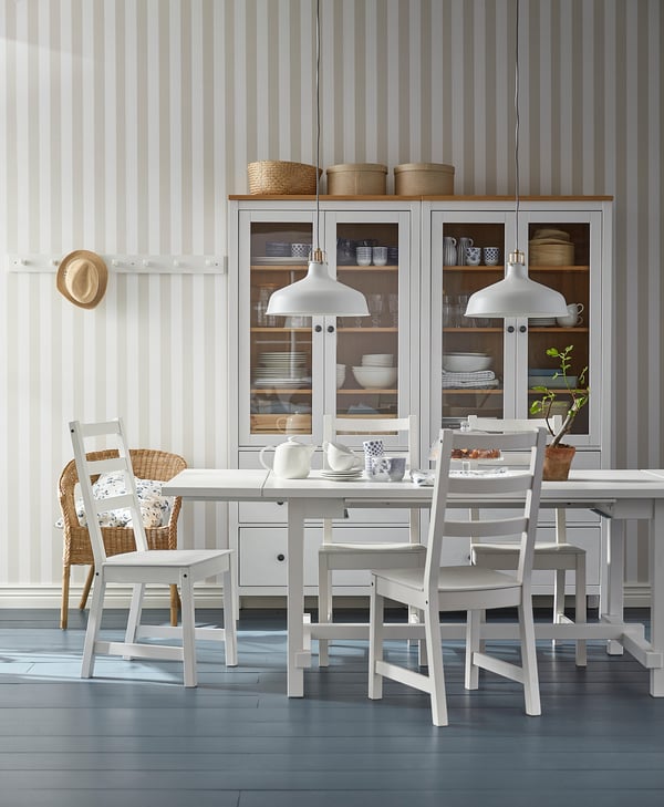 Modern dining set with extendable table, ladder-back chairs, striped wallpaper, pendant lights, and glass cabinet with wicker baskets.