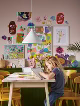 A child drawing at a light birch NORRÅKER table with rounded corners in a colorful room with artistic decorations on green walls.
