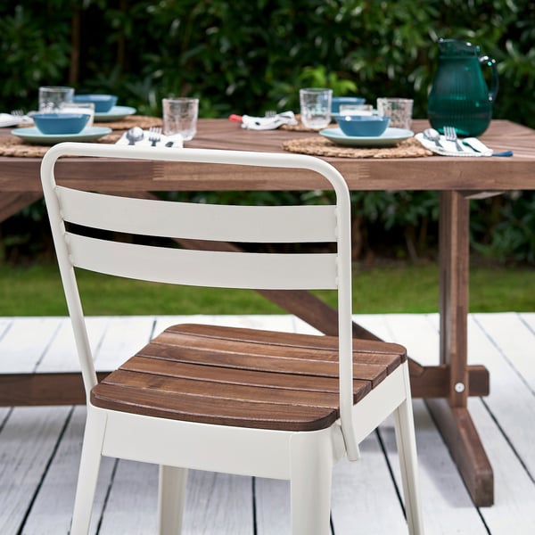 White and wooden NORRMANSÖ patio chair near large outdoor table with matching place settings.