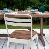 White and wooden NORRMANSÖ patio chair near large outdoor table with matching place settings.