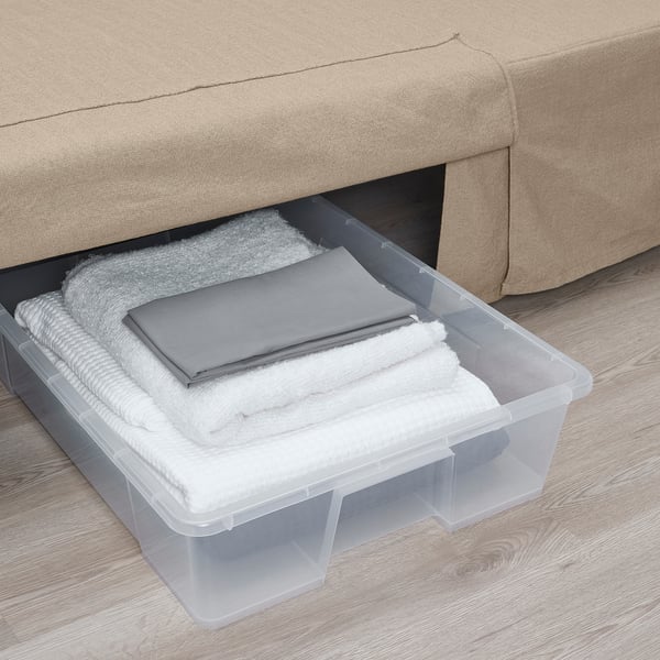 Clear plastic storage box under sofa filled with folded white towels and gray linens.