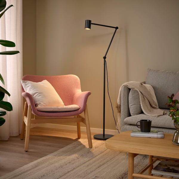 NYMÅNE lamp lights cozy pink chair and beige couch, with black mug and books on wooden table.