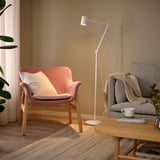 Cozy living room with NYMÅNE floor lamp, light wood, and neutral tones. Pinkish chair, grey sofa, adjustable lamp, wooden coffee table, and rug.