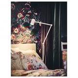 A bedroom with dark floral wallpaper and white metal floor lamp, illuminating floral pillows.