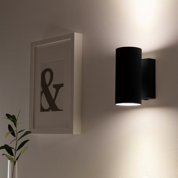 NYMÅNE wall lamp emits soft light, mounted beside ampersand art and a plant.