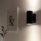 NYMÅNE wall lamp emits soft light, mounted beside ampersand art and a plant.