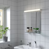 Sleek NYSJÖN mirror on tiled wall, with sink and shelf under sunny window.