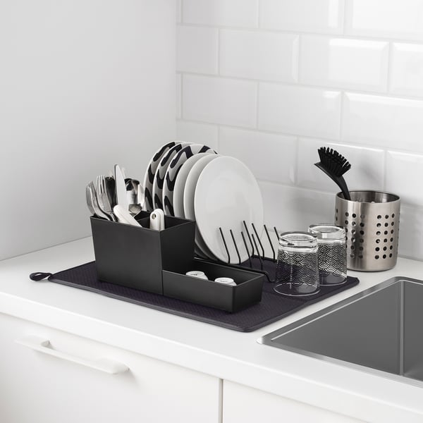 Kitchen sink with dish drainer and drying mat. Drainer holds plates, cutlery, and cups. Mat catches drips.