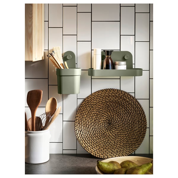 Modern kitchen with green wall organizers holding utensils and items, round woven placemat, wooden utensils in white jar, light tiles.