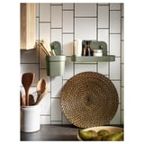 Modern kitchen with green wall organizers holding utensils and items, round woven placemat, wooden utensils in white jar, light tiles.
