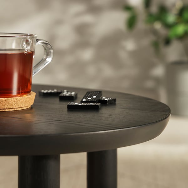 Glass mug filled with tea sits on dark wooden table beside black remote controls.