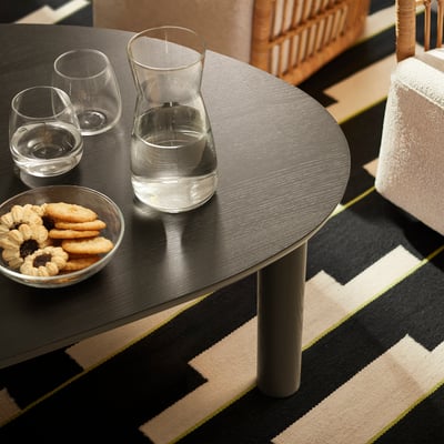Äopy: round table with glasses, cookie bowl, on striped rug. Dark wood, minimalist design.