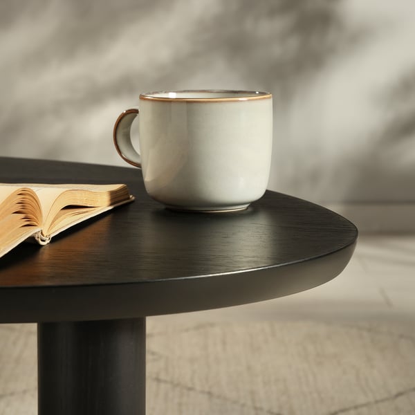 Elegant coffee table with sleek, dark top. Ceramic cup and open book rest on table, showcasing quality and simplicity.