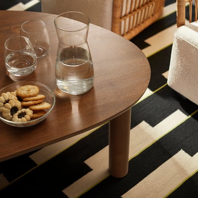 Round wooden coffee table with glass pitcher, three glasses, and a bowl of cookies.