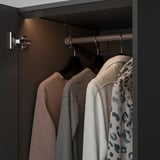 Open wardrobe with illuminated clothes; showing three hangers: beige, grey, and patterned jacket.