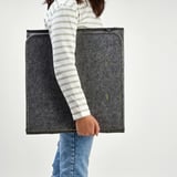 Person holding folded grey desk divider, useful for creating privacy and sound dampening.