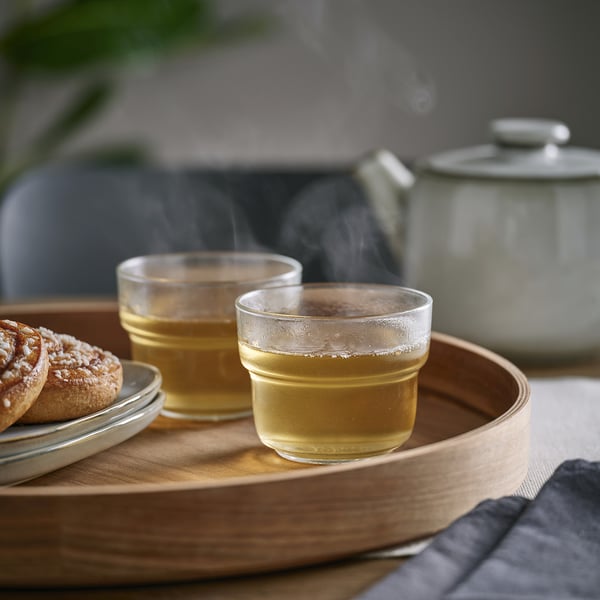 Two glasses of tea on wooden tray, steaming, with a teapot.