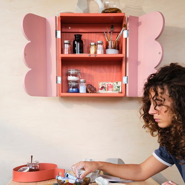 Woman organizing art supplies in a red wall cabinet with shelves.