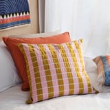 A cozy bed with colorful pillows. A patterned pillow has pink, yellow, and white stripes.