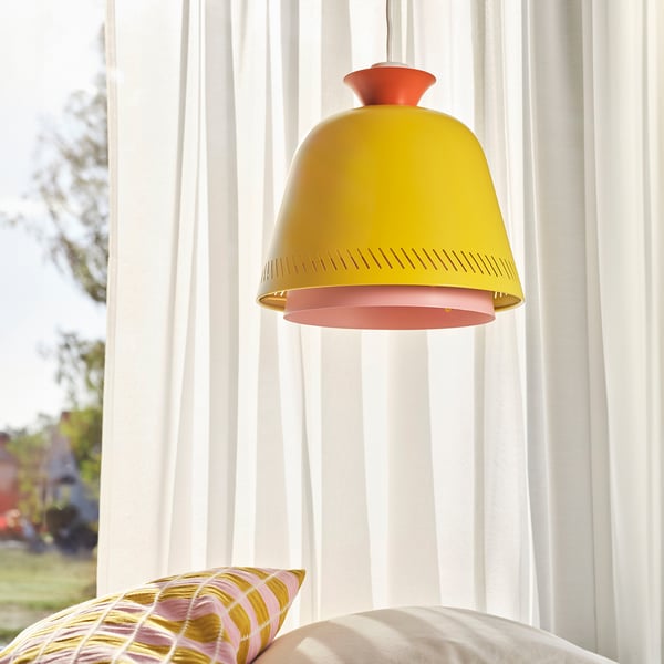 Bright yellow lamp shade hangs by window, casting warm light. Bed below with patterned pillow.