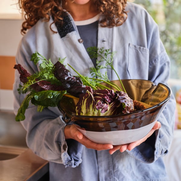 A person holding a large, unique glass bowl, OMMJÄNGE, showcasing its handcrafted beauty.