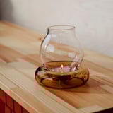 Glass dome candle holder with brown base, warm candlelight, fits in one hand, rustic charm.