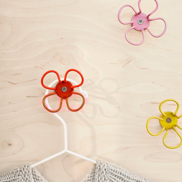 Three colorful flower-shaped wall hooks on a wooden surface, one holding a white cable.