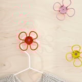 Three colorful flower-shaped wall hooks on a wooden surface, one holding a white cable.