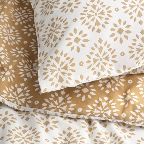 Soft, patterned bedding close-up. Golden flower designs on white and beige. Luxurious, textured reversible duvet cover set.