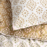 Soft, patterned bedding close-up. Golden flower designs on white and beige. Luxurious, textured reversible duvet cover set.