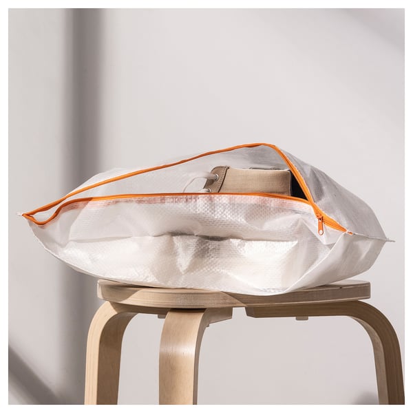 White PÄRKLA shoe bag with orange zipper on wooden stool. Folds flat for easy storage and travel.