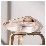 White PÄRKLA shoe bag with orange zipper on wooden stool. Folds flat for easy storage and travel.