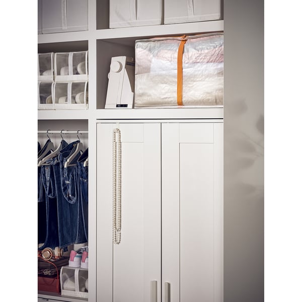 A white parkla storage case, rectangular, holding bedding. Its semi-transparent and stacked on a shelf, fitting neatly beside other items.