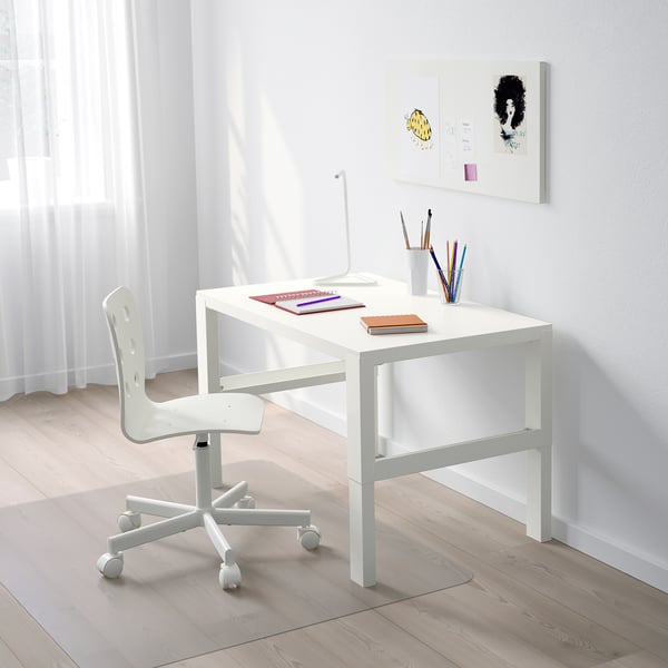 A small white adjustable desk with wheels, a chair, and colorful school supplies, positioned under a window with light curtains.