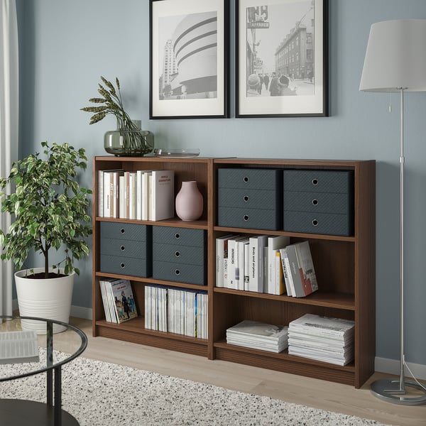 Wooden PALLRA storage unit with grey drawers against blue walls, holding books and decor. Lamp, plant, and photos nearby.