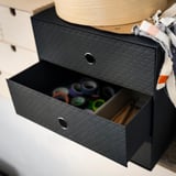 Black PALLRA storage box, open showing colorful items, black textured exterior, metal handles.