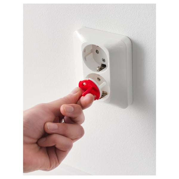 Hand inserts red key into white wall socket protector, ensuring child safety.
