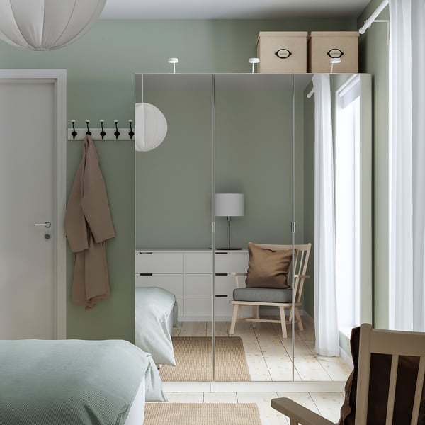 Modern bedroom with green PAX wardrobe, mirrors, blue bed, chair, coat hooks, natural light.