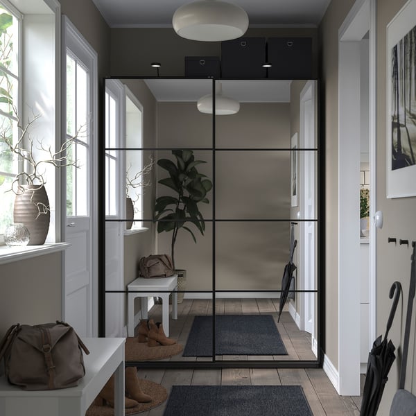 Modern entryway with glass-walled closet, featuring sliding doors, white decor, and potted plant.
